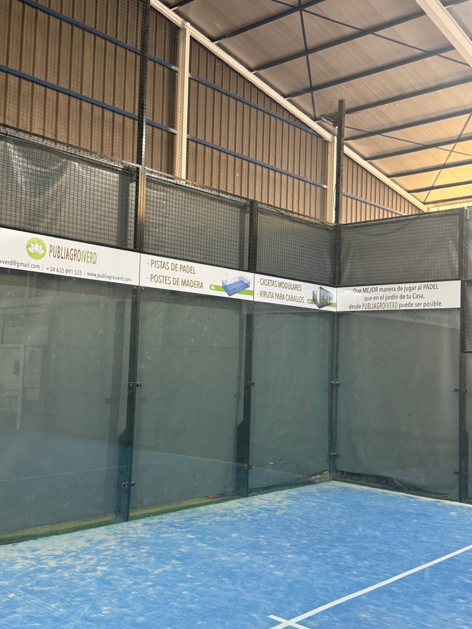 Interior de pista de pádel con césped azul y cartel de PUBLIAGROIVERD