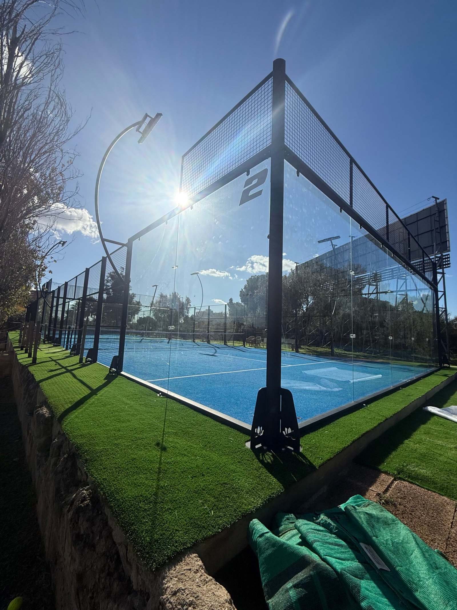 Pista de pádel con suelo azul y palmeras instalada por PUBLIAGROIVERD