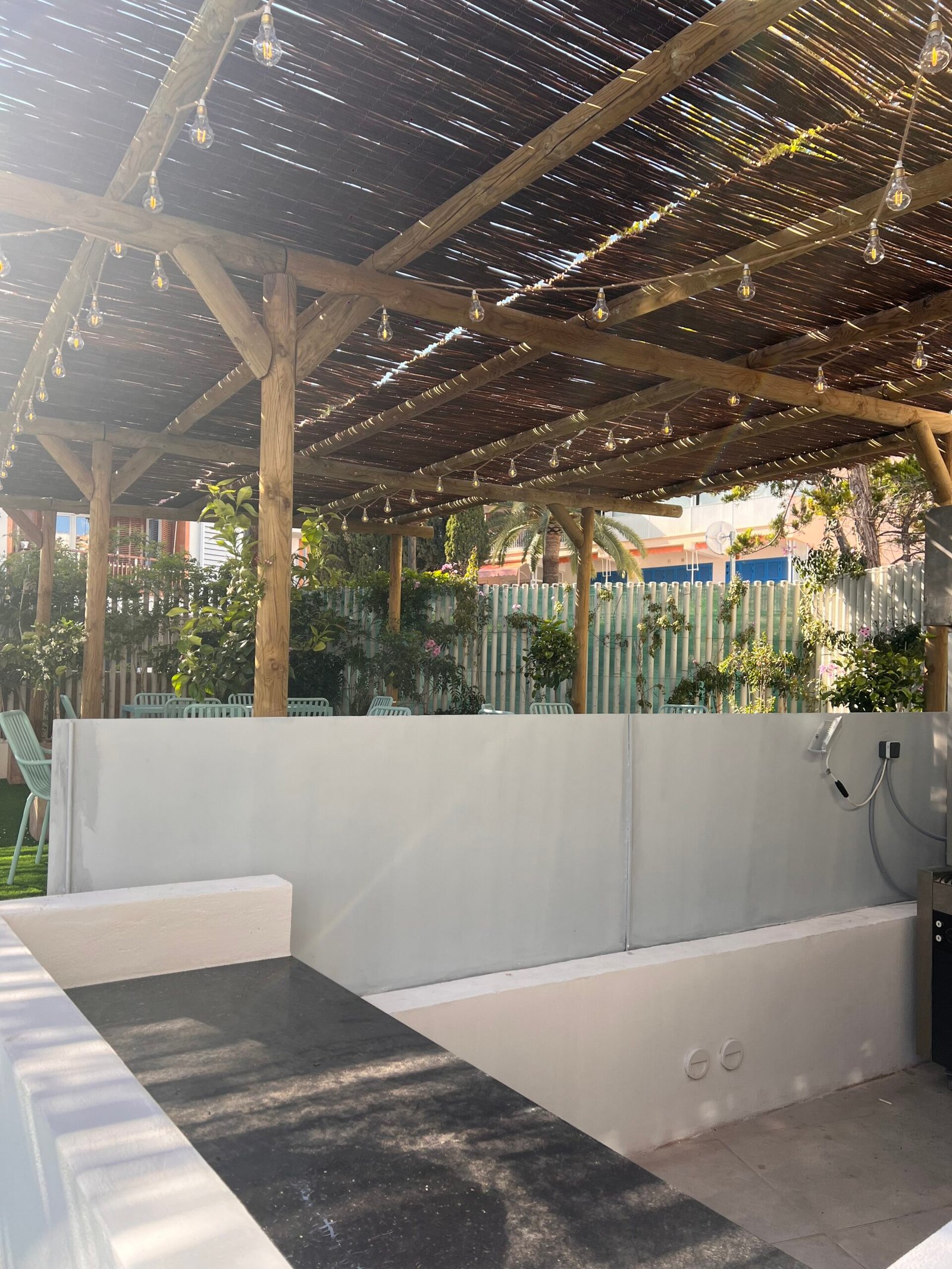 Pérgola con techo de cañizo y luces colgantes junto a zona de barbacoa