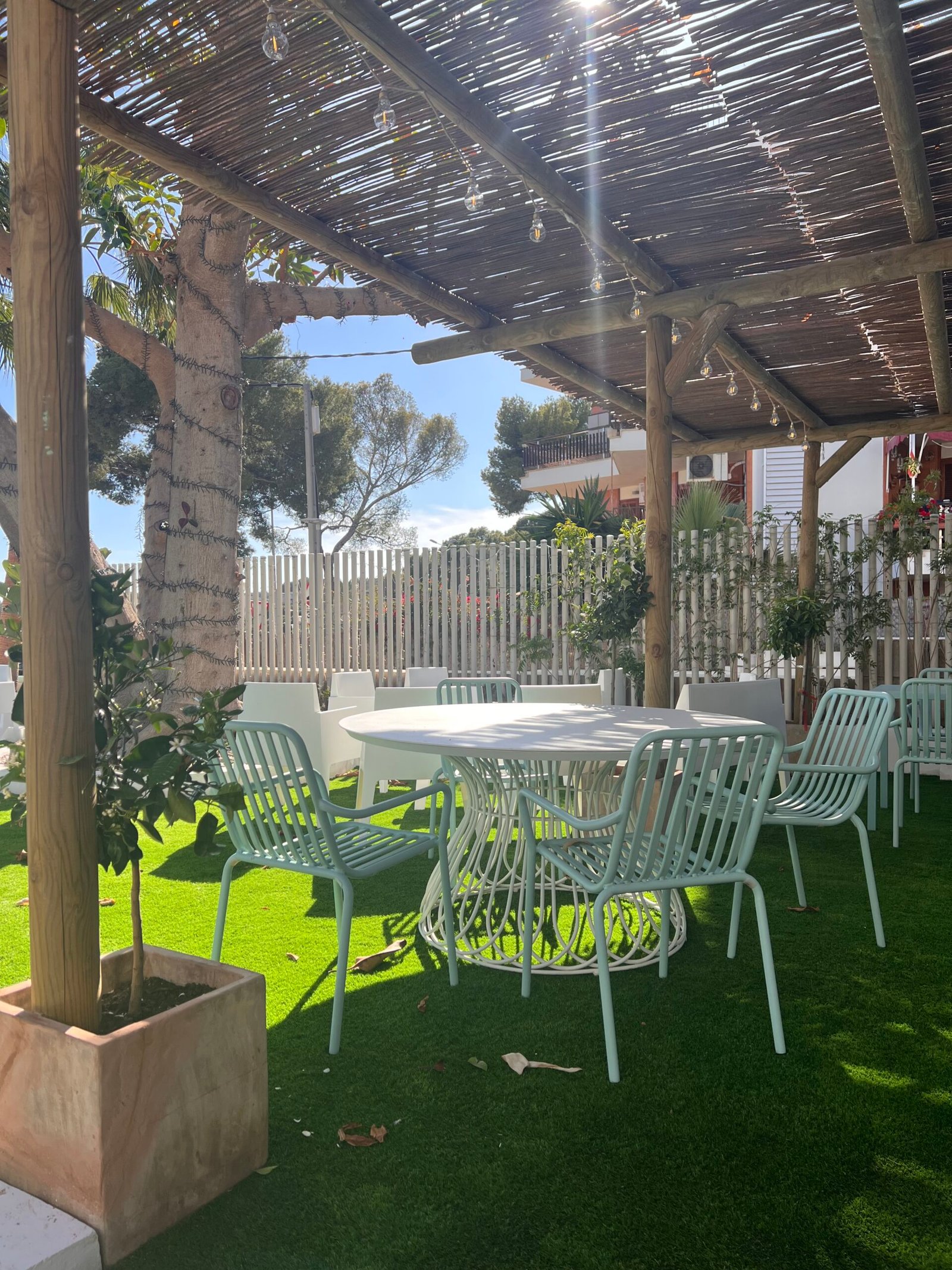 Pérgola con techo de cañizo, mesa y sillas verdes sobre césped artificial