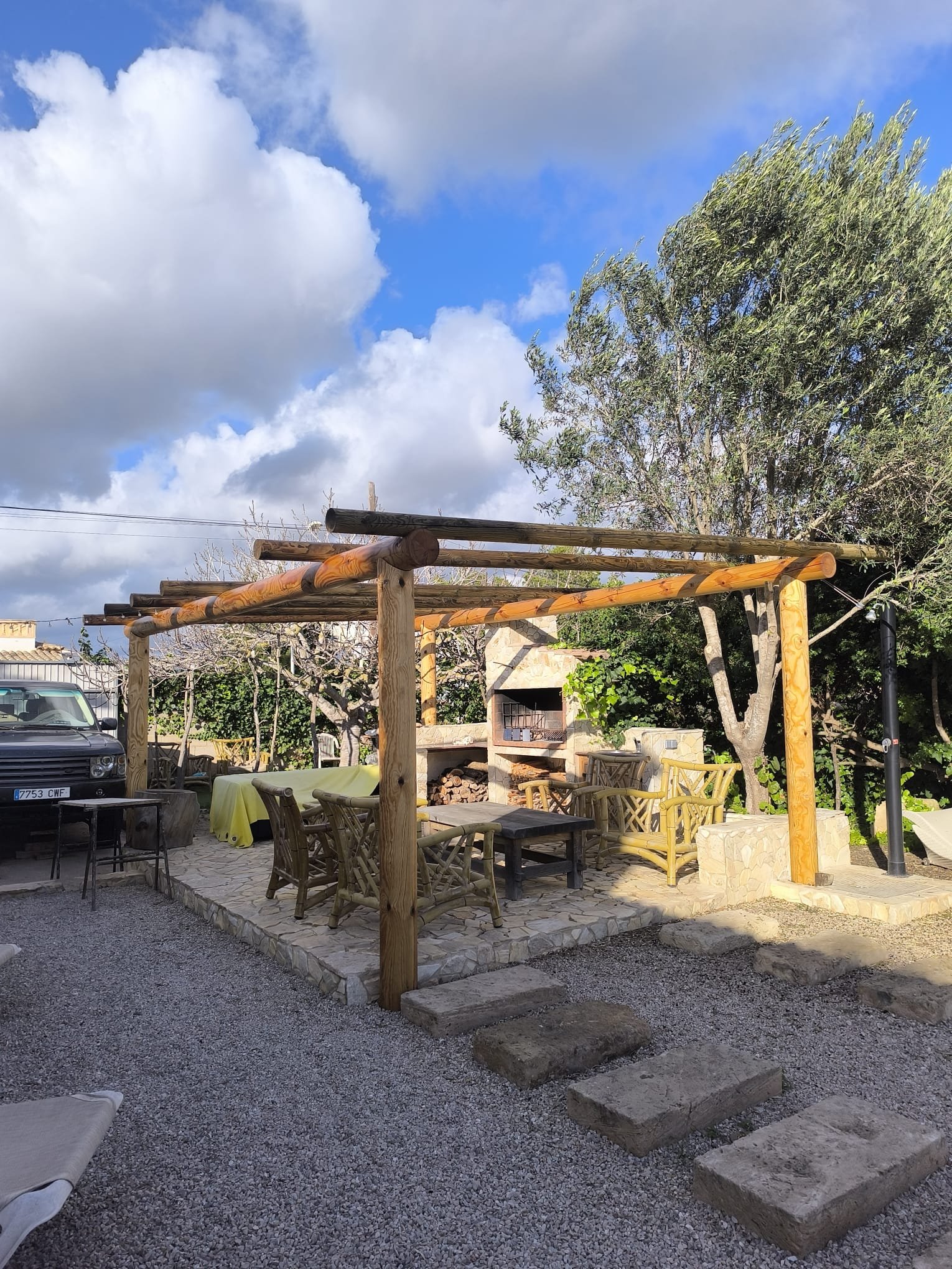 Pérgola de madera con barbacoa de piedra y zona de estar bajo olivo