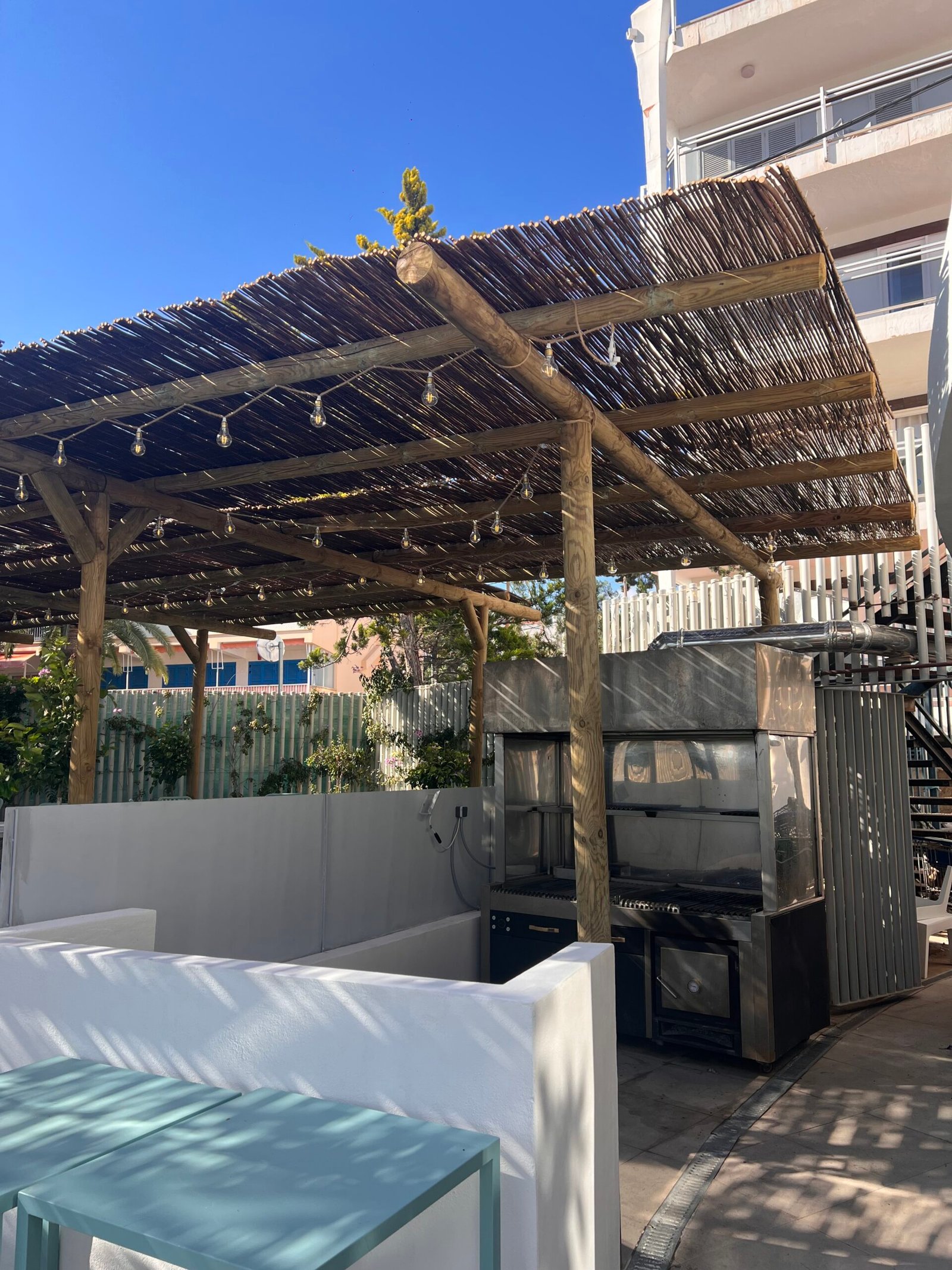 Pérgola con techo de cañizo sobre terraza con ducha y parrilla de acero inoxidable