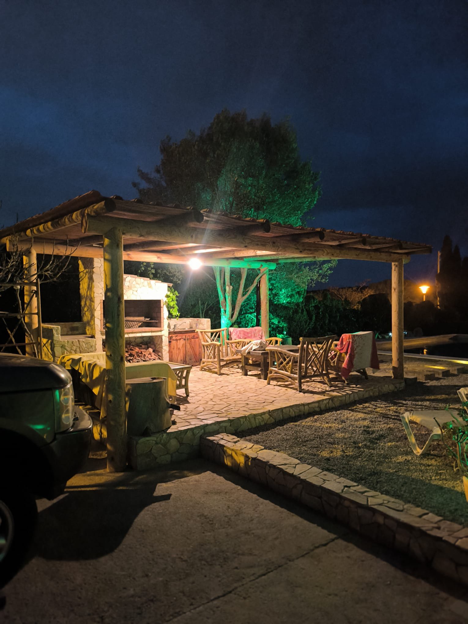 Pérgola con iluminación decorativa verde de noche junto a piscina