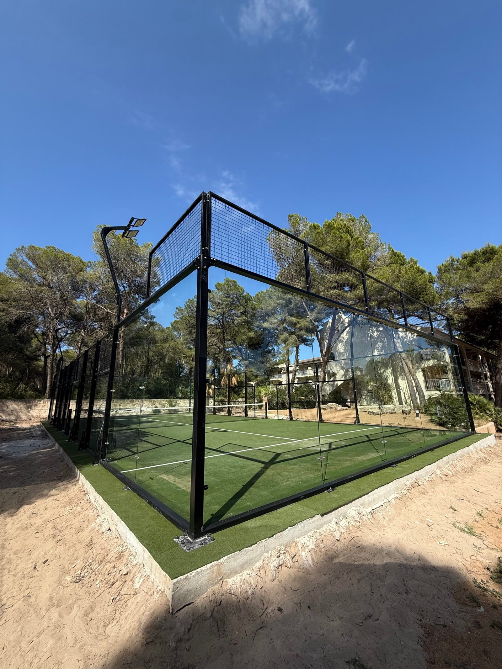 Pista de pádel con césped verde y estructura de cristal entre pinos